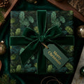 Elegant Christmas gift wrapped in evergreen tree print paper, secured with a velvet green ribbon and "Merry Christmas" tag.