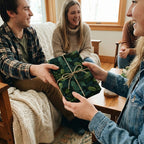 Friends exchanging a gift wrapped in Christmas wrapping paper with green pine needles and twine.