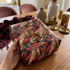 Luxury gift wrapped in autumnal leaf wrapping paper, tied with gold string.