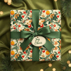 Square gift wrapped in floral Christmas wrapping paper with green satin ribbon and "Joy & Cheer" tag.