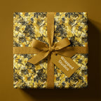 Square gift wrapped in yellow floral wrapping paper with a gold ribbon and Wrapped Studios tag.