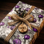 Luxury Christmas gift wrap with purple ornaments and a rustic "Noel" tag, tied with a burlap ribbon.