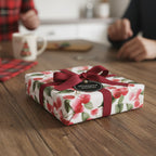 Square gift wrapped in floral wrapping paper with red ribbon on wooden table.