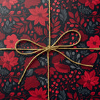 Close-up of a gift wrapped in red floral Christmas wrapping paper with a gold cord bow.