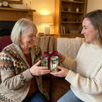 Wrapped Studios luxury winter village gift wrap with red velvet bow on a present exchanged by two women.