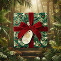 Square gift wrapped in green floral Christmas wrapping paper with red velvet bow, and "Happy Holidays!" tag.