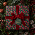 Luxury Christmas gift wrap: Floral leaf pattern with red velvet ribbon and "Season's Greetings" tag.