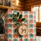 Vintage Christmas wrapping paper with red and blue bows and a wood Joy tag by Wrapped Studios.