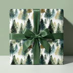 Square gift wrapped in watercolor forest tree wrapping paper, tied with a green satin ribbon.