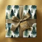 Square gift with evergreen tree print wrapping paper, gold ribbon, and "from our forest to yours" tag.