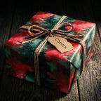 Christmas gift wrapped in red and green watercolor paper with twine bow and 'Cheers' tag.