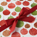 Festive Christmas gift wrap with a playful ornament pattern in red, green, and brown, tied with an elegant red satin bow.