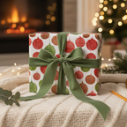 Christmas gift box in festive red and green ornament wrapping paper with a green velvet ribbon, cozy holiday decor background.