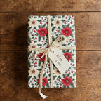 Floral Christmas gift wrap featuring red poinsettias, tied with a cream velvet ribbon and "With Love" tag.