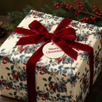 Christmas gift wrapped in festive botanical wrapping paper, tied with a red velvet ribbon.