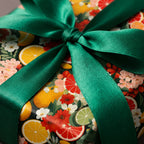 Close-up of floral wrapping paper with orange and grapefruit design, finished with a luxurious green satin ribbon.