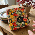 Gift box with floral and citrus design on a wooden table, featuring 'Wrapped Studios' branding.