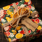 Handpicked gift wrapped in colorful citrus floral wrapping paper with dried orange slice and cinnamon stick detail.
