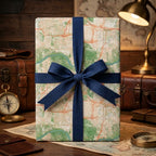 Vintage map wrapping paper with a navy blue ribbon bow by Wrapped Studios, on a rustic travel-themed desk.
