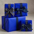 Stack of elegant blue gift boxes wrapped in solid color paper with dark ribbon bows.