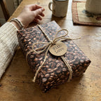 Rectangle gift with coffee bean wrapping paper, twine bow, and "With Love" tag on a wooden table.