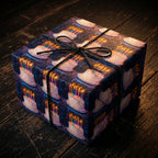 Birthday wrapping paper featuring a cake and candle pattern, tied with black string on a dark wood surface.