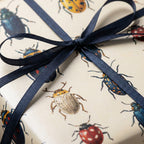 Elegant gift wrapped in beige paper with an insect pattern and tied with a navy blue ribbon.