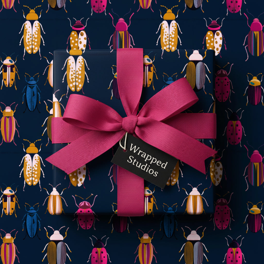Navy gift box wrapped in colorful beetle print paper with bright pink ribbon and "Wrapped Studios" tag.