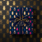 Navy gift wrap with colorful beetle pattern, tied with navy ribbon and gold accents; elegant wrapping paper.