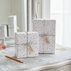 Modern polka dot wrapping paper on two white gift boxes with silver twine and "Wrapped Studios" tags, on a vanity with a mirror and pearls, perfect for birthday or baby shower gifts.