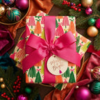 Colorful Christmas tree wrapping paper with a pink bow and holiday gift tag by Wrapped Studios.