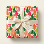 Colorful Christmas tree wrapping paper with a white satin bow by Wrapped Studios.