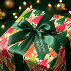 Colorful Christmas tree wrapping paper with a dark green satin bow and a Wrapped Studios tag.