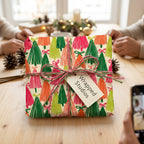 Colorful Christmas tree wrapping paper by Wrapped Studios on a gift tied with twine at a holiday table.