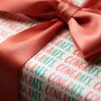 Congratulations wrapping paper with coral and teal text and a matching satin ribbon bow by Wrapped Studios.