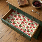 Vintage Christmas gift wrap with red bows and holly lining a rustic drawer by Wrapped Studios.