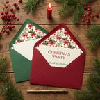 Red and green Christmas envelope liners with festive holly patterns on rustic wood by Wrapped Studios.