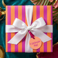 Pink and orange striped birthday wrapping paper with a white satin bow and gift tag by Wrapped Studios.
