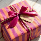 Orange and purple striped wrapping paper with a pink ribbon and handmade tag by Wrapped Studios.