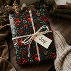 Elegant floral gift wrap with red berry accents, tied with twine and "Joy" tag.