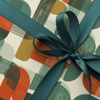 Modern gift wrap with abstract orange and green shapes, tied with a dark teal satin ribbon.