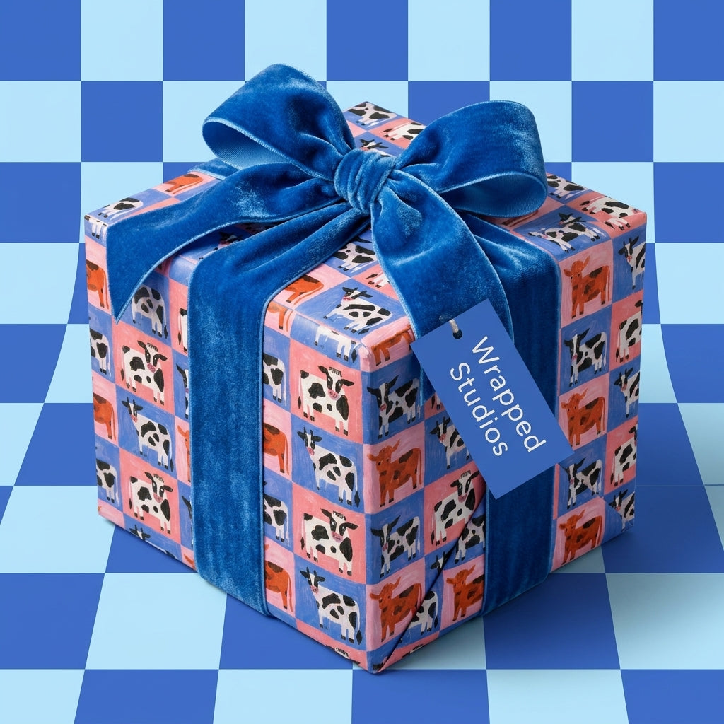 Cute cow print wrapping paper with a blue velvet ribbon on a gift box by Wrapped Studios.