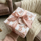 Pink teddy bear baby shower wrapping paper with a satin bow and 'Hugs & Kisses' tag by Wrapped Studios.