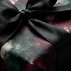 Luxury abstract gift wrap in moody green and burgundy with a black satin bow by Wrapped Studios.
