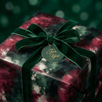 Luxury Christmas wrapping paper in a moody green and burgundy abstract print with velvet bow by Wrapped Studios.