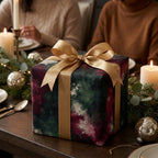 Luxury Christmas gift wrap in abstract green and red with a gold ribbon on a holiday table by Wrapped Studios.