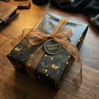 Elegant dark gift wrap with glowing building pattern and bronze ribbon from Wrapped Studios.