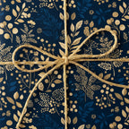 Navy blue gift box wrapped in gold floral wrapping paper with a gold twine bow.