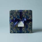 Elegant gift box wrapped in navy floral wrapping paper with gold accents and navy ribbon.
