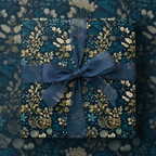 Elegant gift wrapped in dark teal floral wrapping paper, accented with a sheer blue ribbon and bow.